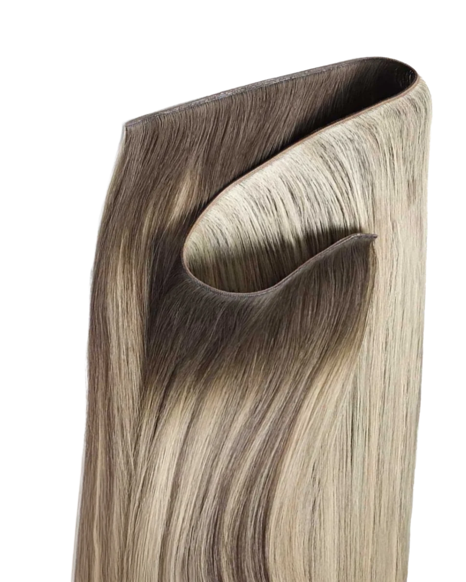 A close-up of a hair extension or wig tip showing a blended color gradient from dark ash brown to light ash blonde, with a cut, layered end, on a solid white background.